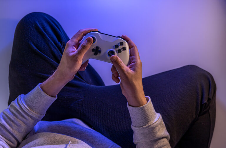 Male hands hold a gamepad on a blue background, copy space.